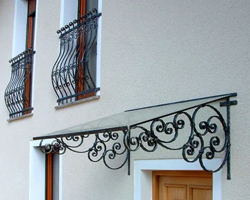 Kovan nadstrešek je narejen iz istih materialov kot ograje na francoskih balkonih in usklajen z vrtno ograjo na