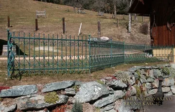 Zeleno patinirana kovana ograja na travniku preprečuje padec po skalah lepega skalnjaka