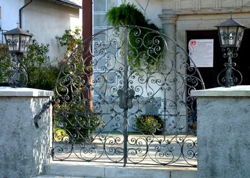 Bogata polkrožna vrata v cerkvenem obzidju in kovane laterne