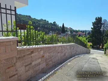 Kovane ograje na kamnitem zidu ob strmi ulici v Portorožu